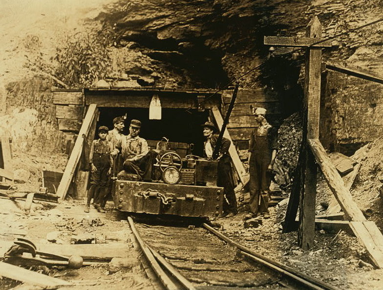 Entrance to a W. Va. coal mine: a "drift" mine. The live-wire was only shoulder -high in places inside, and unprotected. Location: West Virginia. Source: https://commons.wikimedia.org/wiki/File:W._Va._coal_mine_1908.jpg
